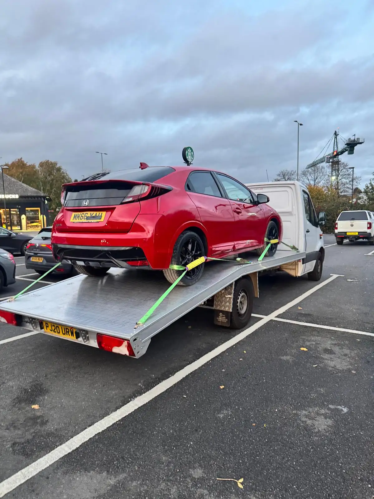 Red hatchback car secured on a white recovery truck in a parking lot, ready for transport